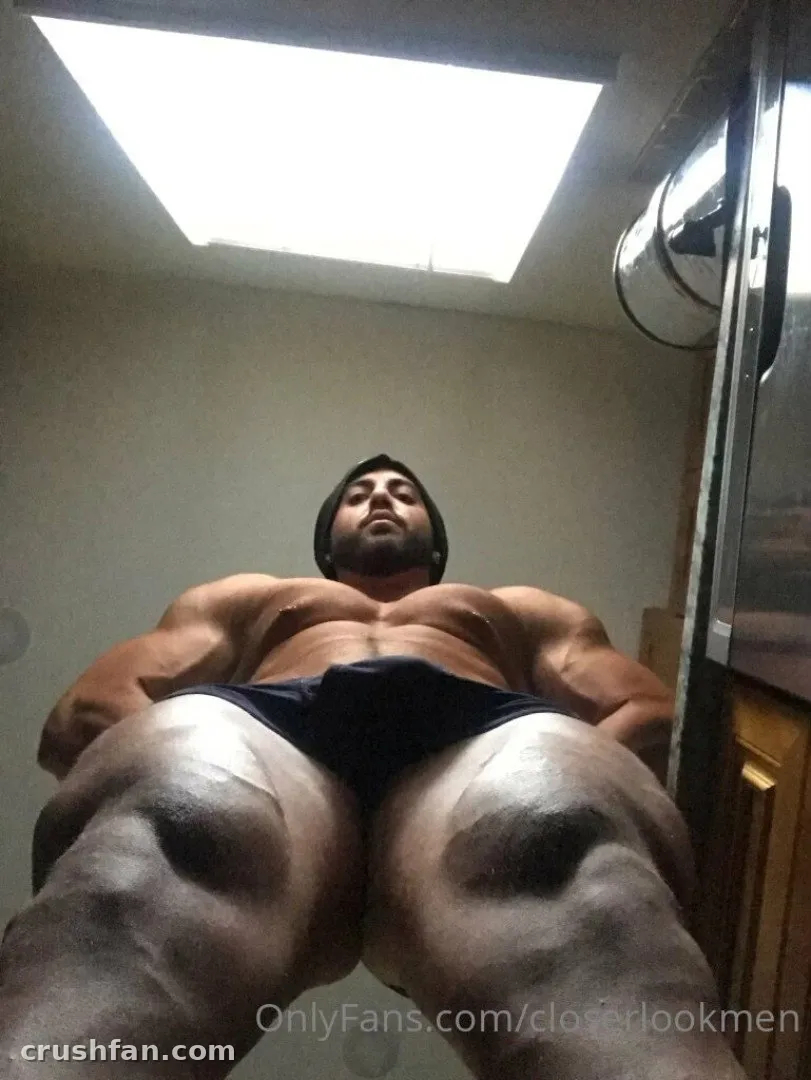 Homem musculoso de cueca escura e blusa escura posando em uma sala interna bem iluminada