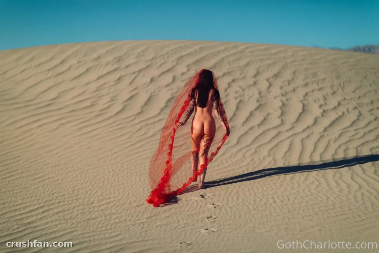 Goth Charlotte walking a sand dune with a long red veil trailing behind her