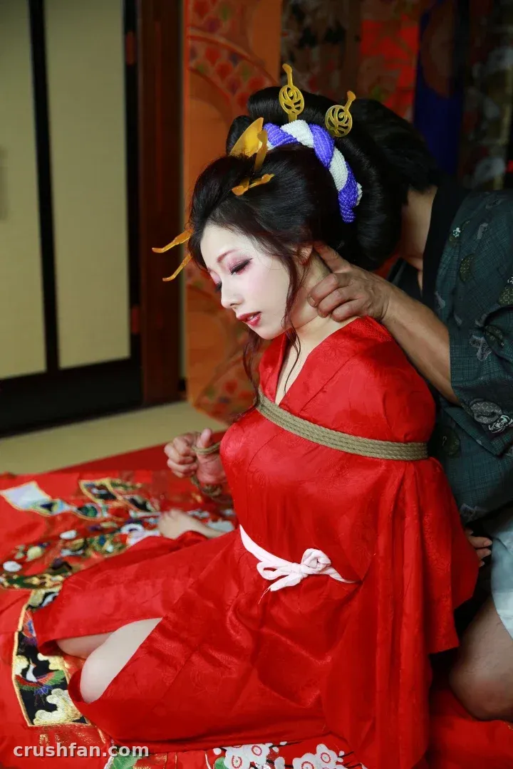 Tunamayo seated in a red kimono with gold hairpins in a warm traditional room