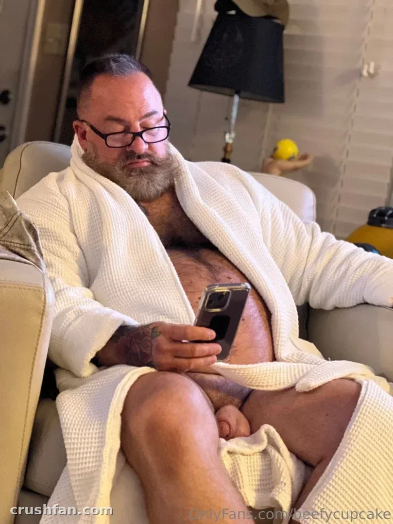 BeefyCupCake in a white robe looking at a phone while seated indoors.