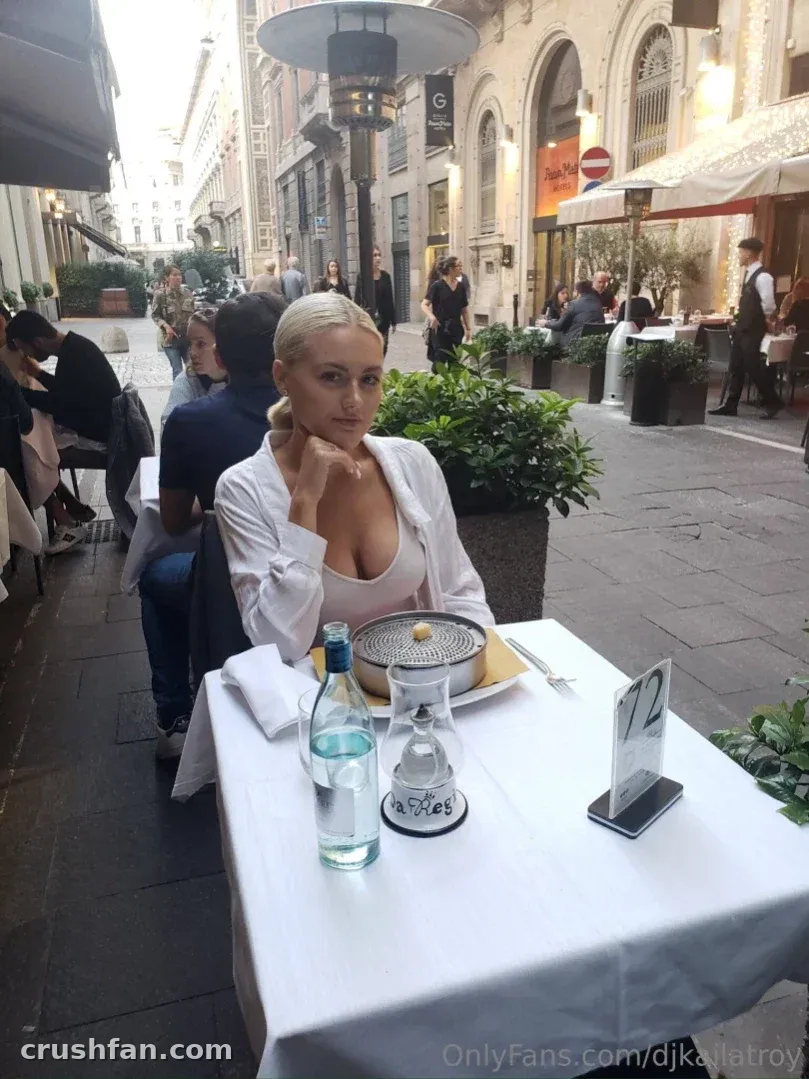 Kaila Troy sitzt in einem weißen Hemd an einem Tisch in einem Outdoor-Café und blickt in die Kamera.