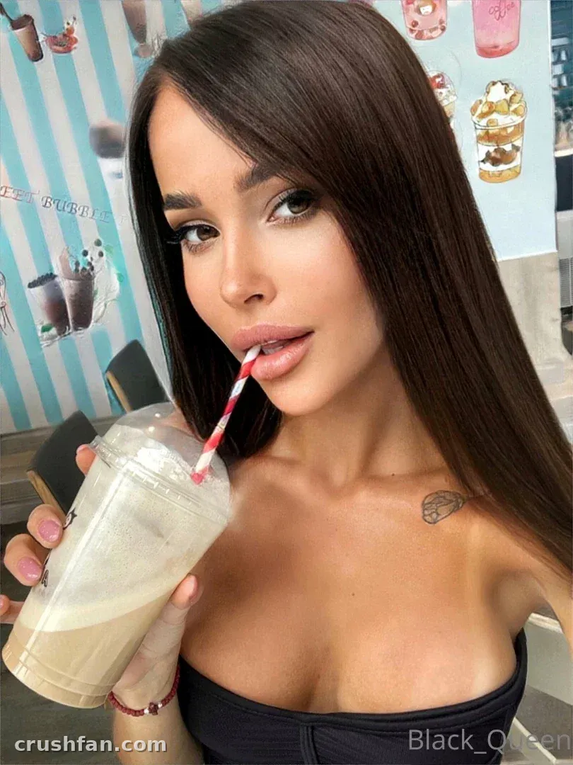 Darina in a black strapless top holding an iced drink with a striped straw in a bright cafe