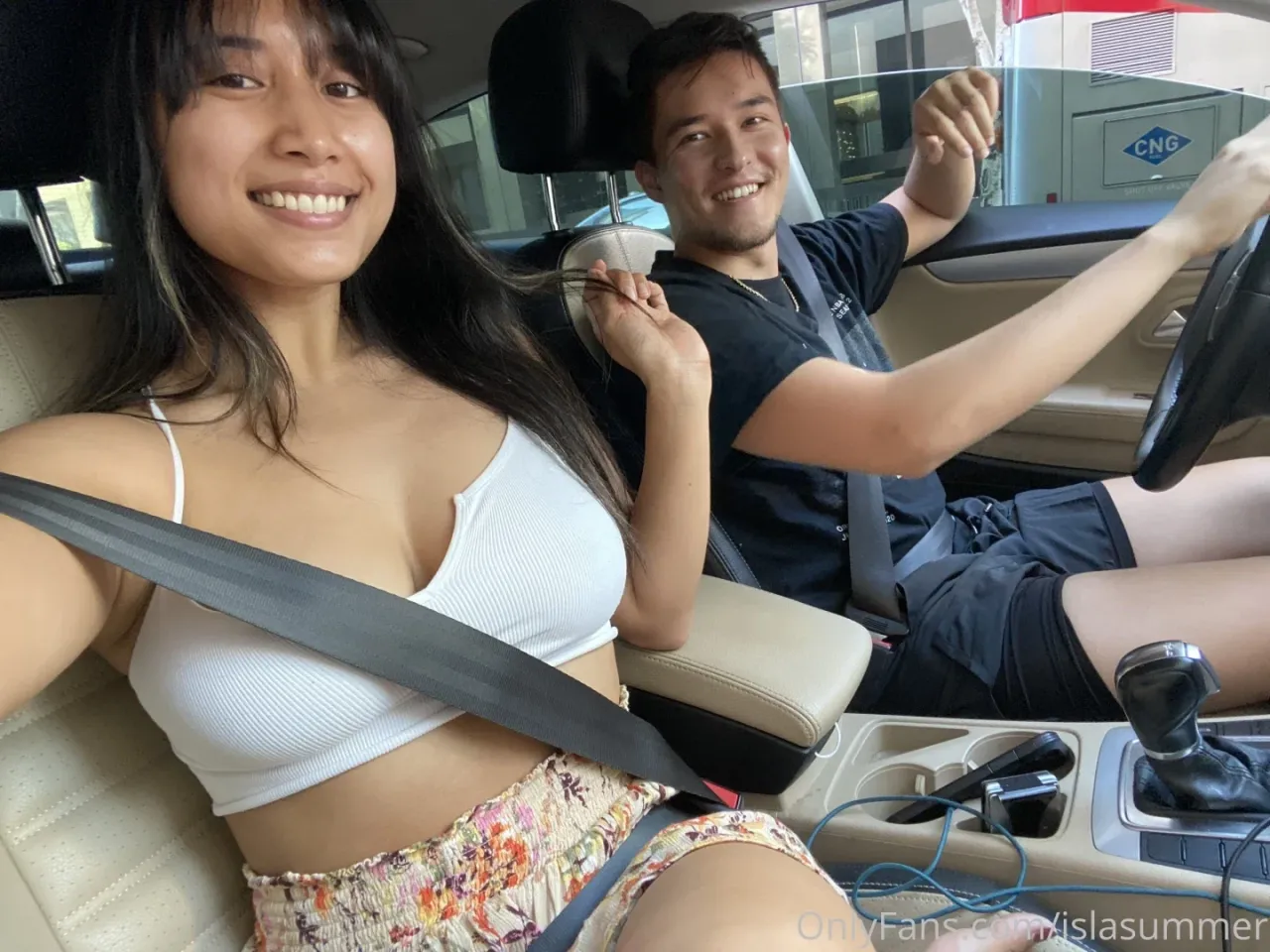 Isla Summer com um top cropped branco sorrindo dentro de um carro durante um passeio diurno