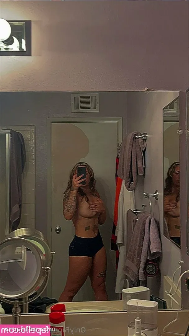 Roxanne prenant un selfie dans le miroir dans une salle de bain avec des serviettes suspendues à proximité