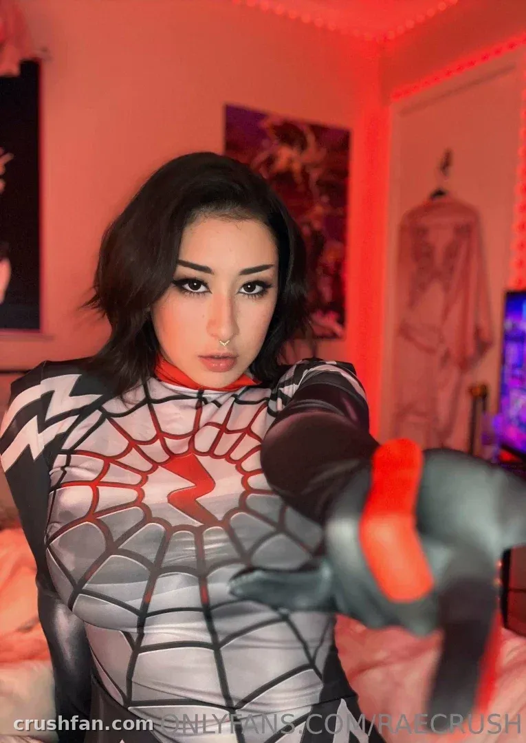 Rae in a black and silver web-patterned costume under red indoor lighting