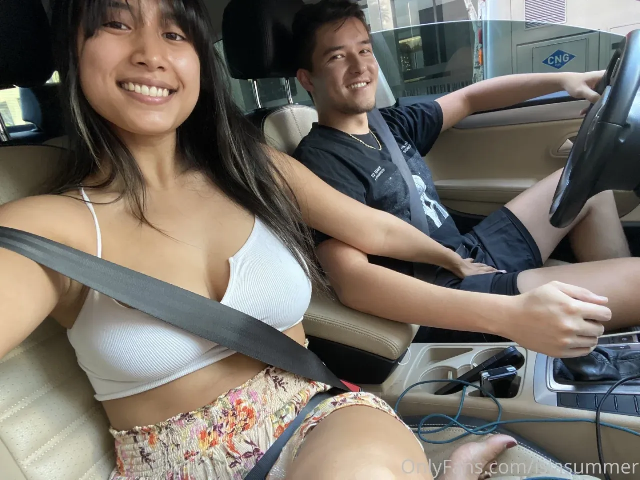 Isla Summer sonriendo en una selfie en el coche con un top blanco y una falda floral