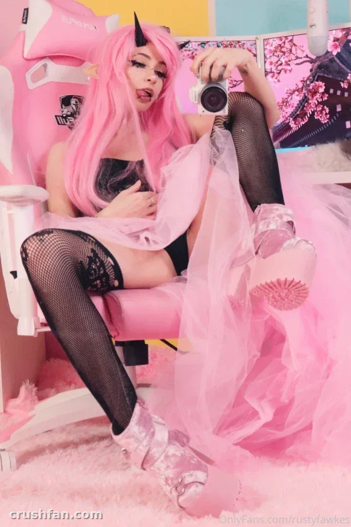 Creadora con peluca rosa y medias de rejilla sentada en una silla gamer rosa sosteniendo una cámara