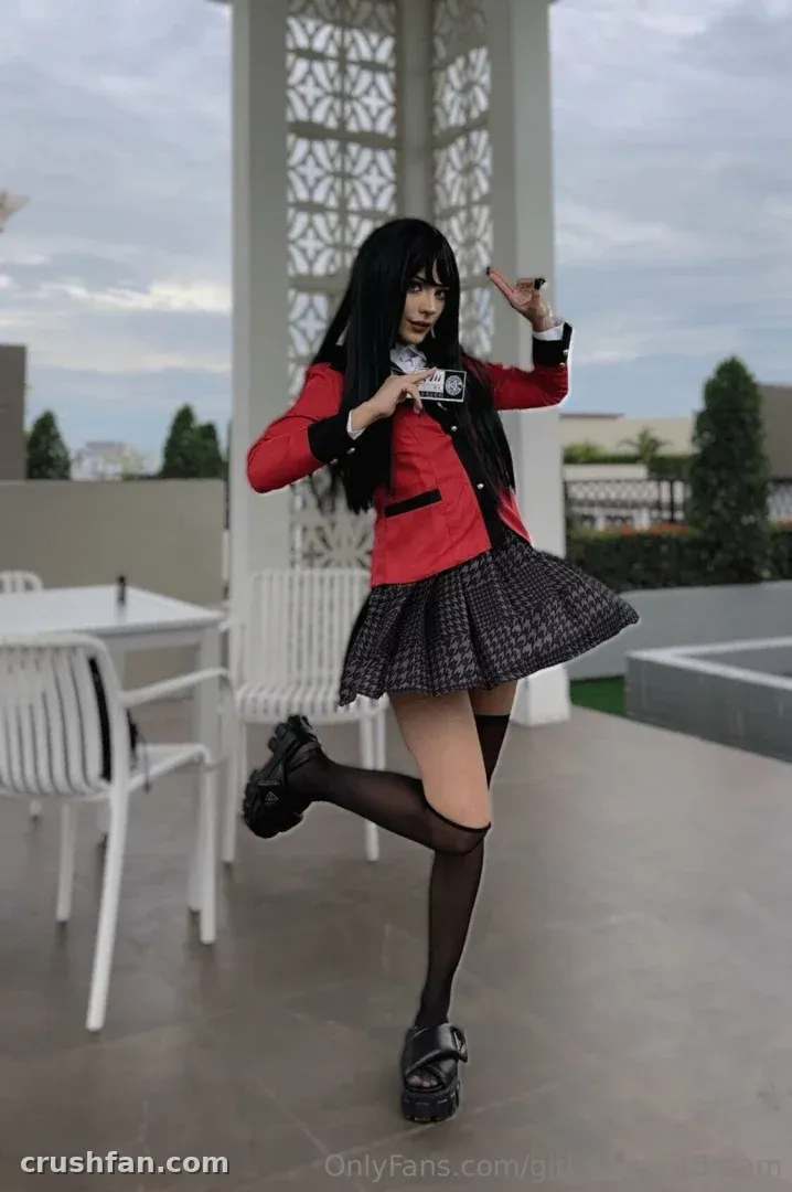 Daisy in a red blazer and checked skirt posing on an outdoor terrace.