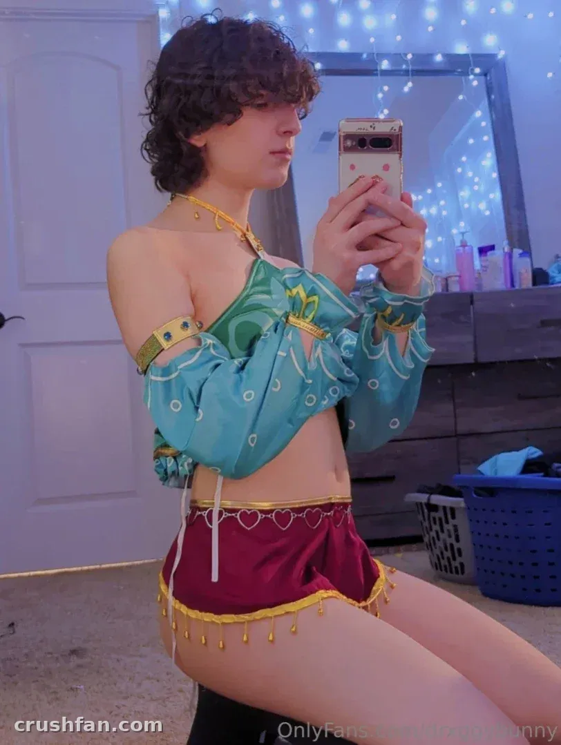 Vinny in teal and gold cosplay outfit taking a mirror selfie in a softly lit room.