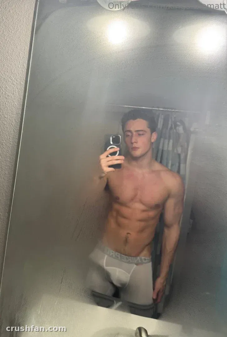 Criador sem camisa de cueca cinza tirando uma selfie no espelho em um banheiro.