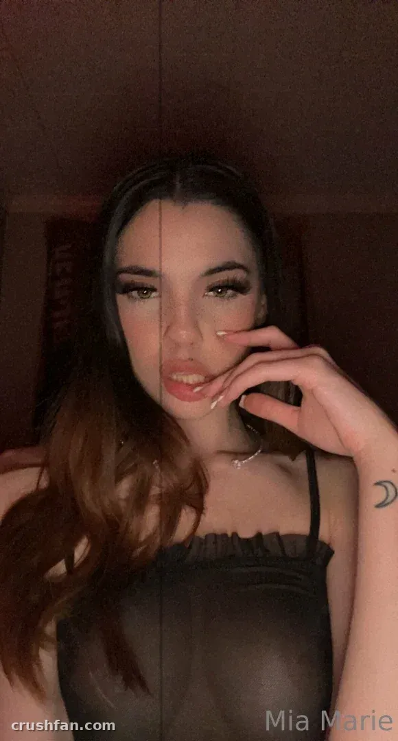Mia Marie in a dark strappy top posing indoors in low warm light