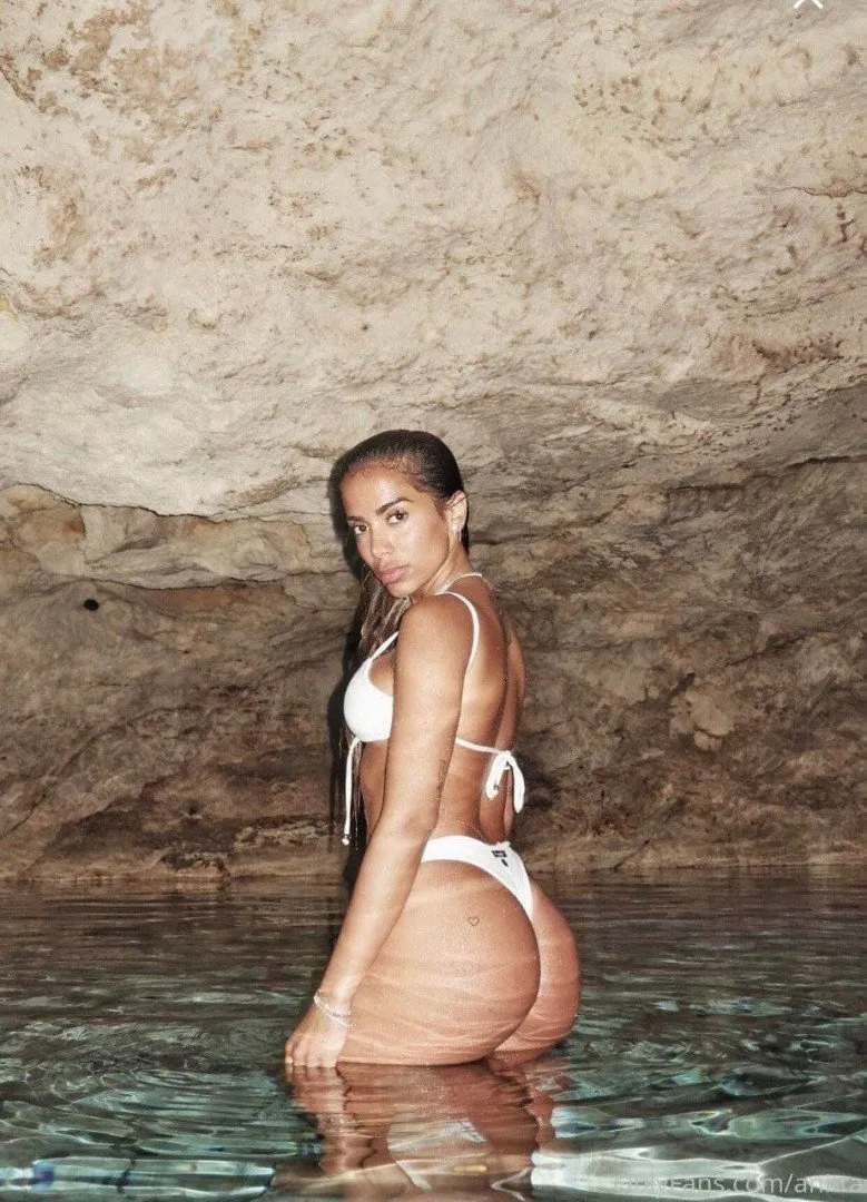 Anitta de biquíni branco em pé na água dentro de uma caverna rochosa