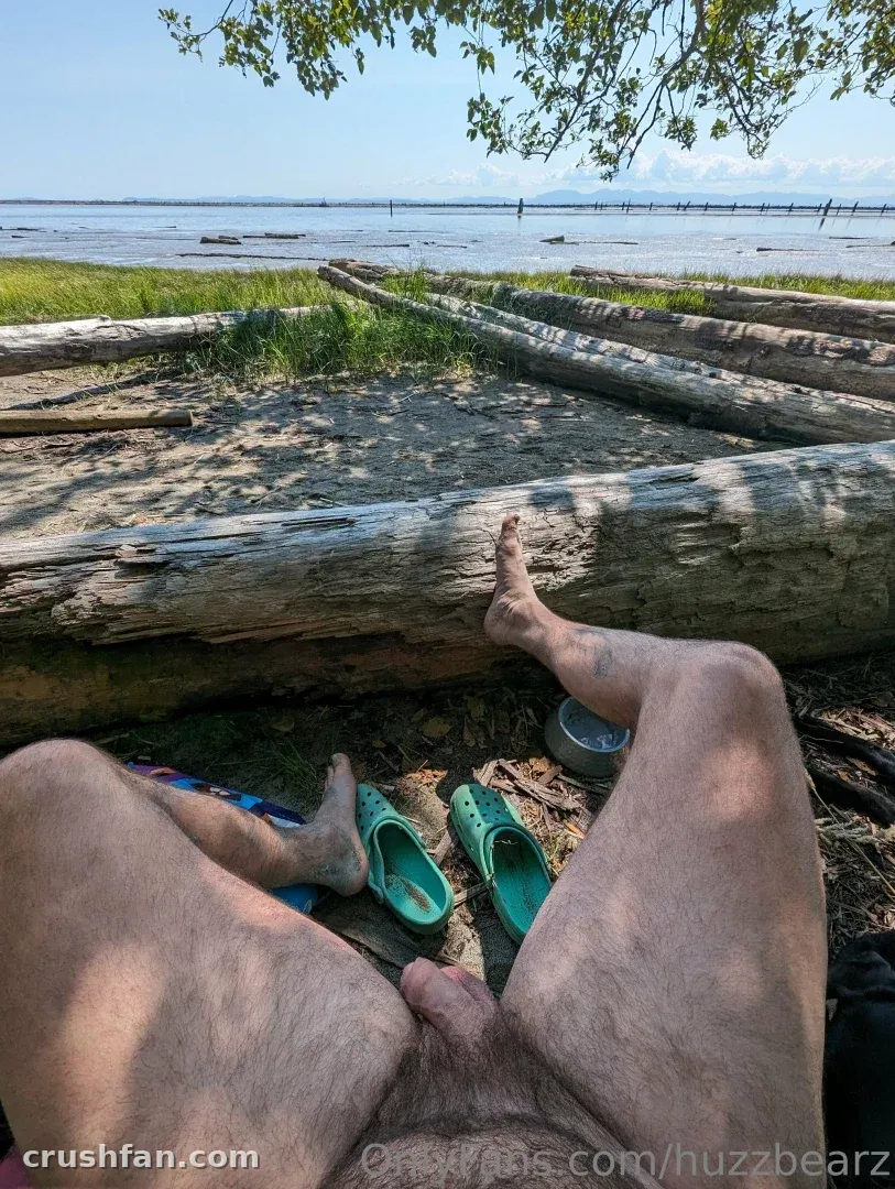 Piernas desnudas descansando sobre un tronco de madera flotante junto al agua con sandalias verdes cerca