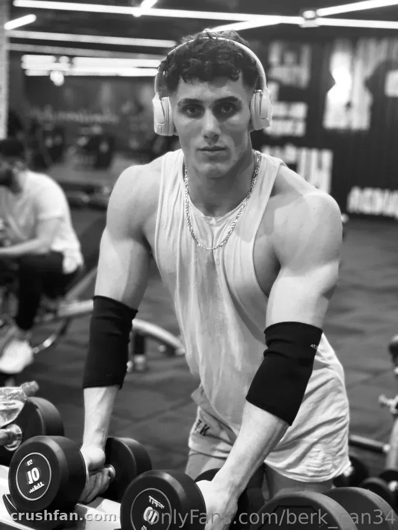 Mr. Berk in a black and white gym photo holding dumbbells while wearing headphones and a tank top.