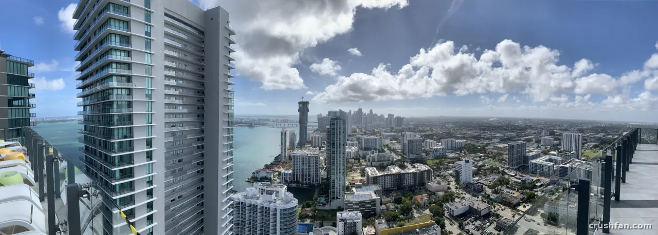 Wide city skyline seen from a high balcony with glass railings under a cloudy blue sky