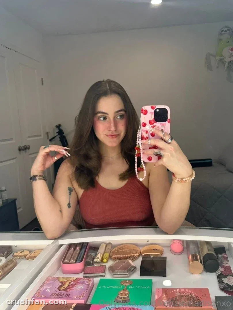 Creadora con una camiseta de color rojo óxido sosteniendo una funda de teléfono rosa frente al espejo de un tocador de maquillaje.