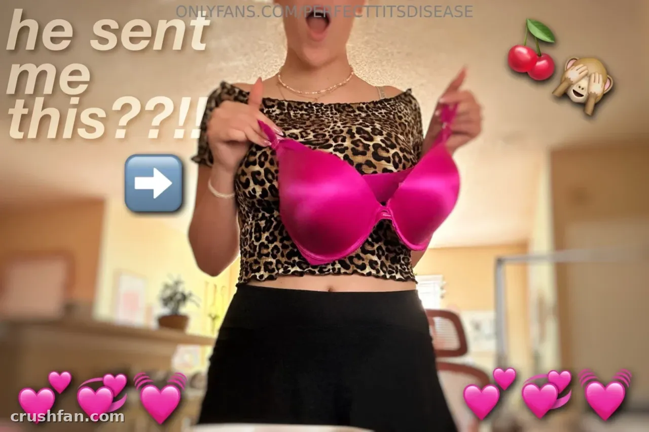 Natalia Love de top de leopardo segurando um sutiã rosa brilhante à sua frente em ambiente interno
