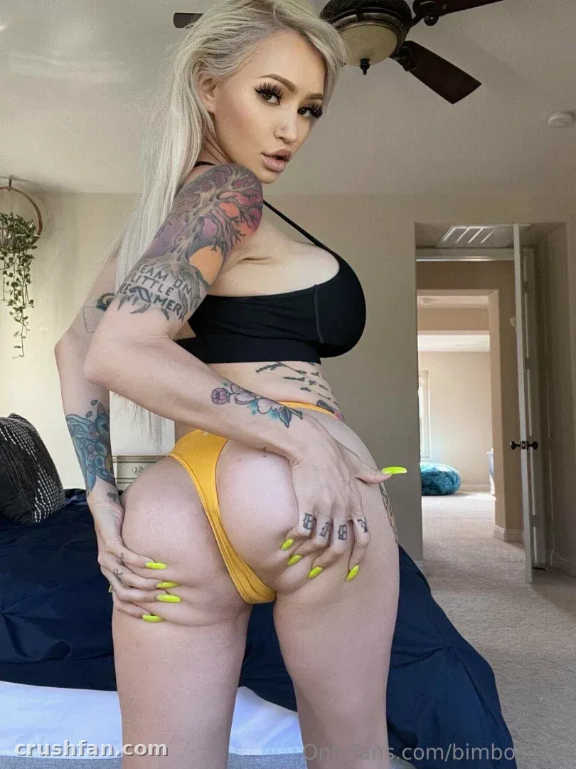 Créatrice en haut noir et bas jaune debout dans une chambre avec des tatouages visibles