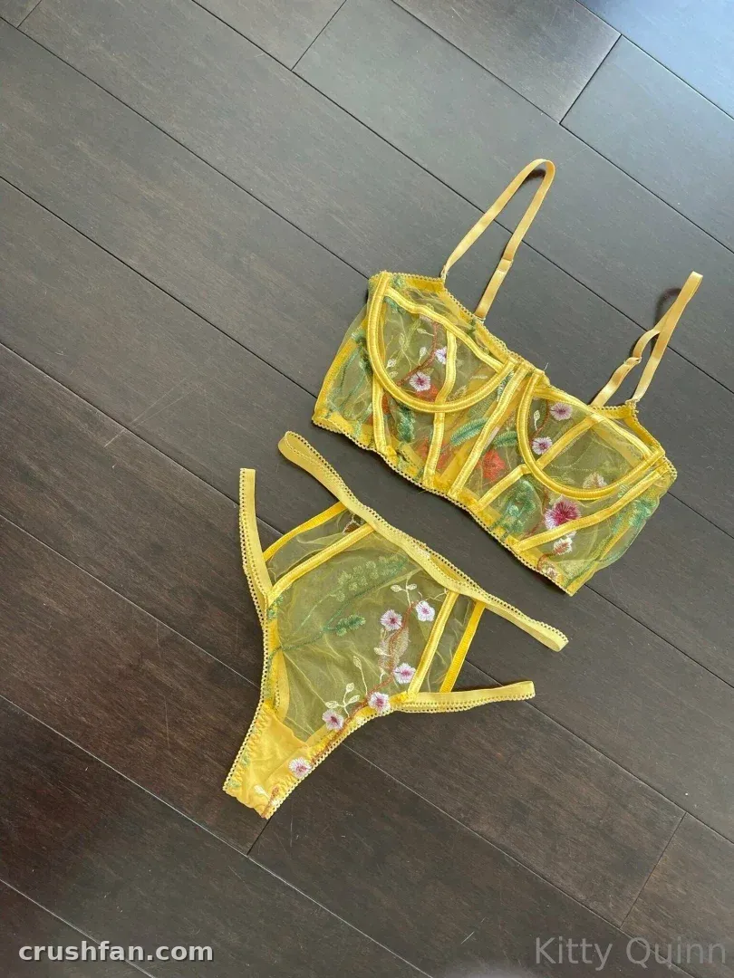 Conjunto de lencería amarilla transparente con flores colocado plano sobre suelo de madera oscura.