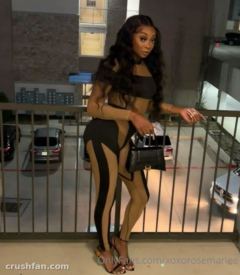 Persuasian on a balcony at night in a black and nude outfit holding a small handbag