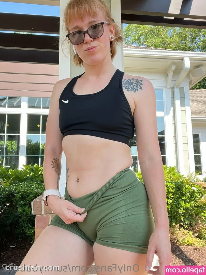 Woman in a black crop top and olive shorts standing outdoors by a building