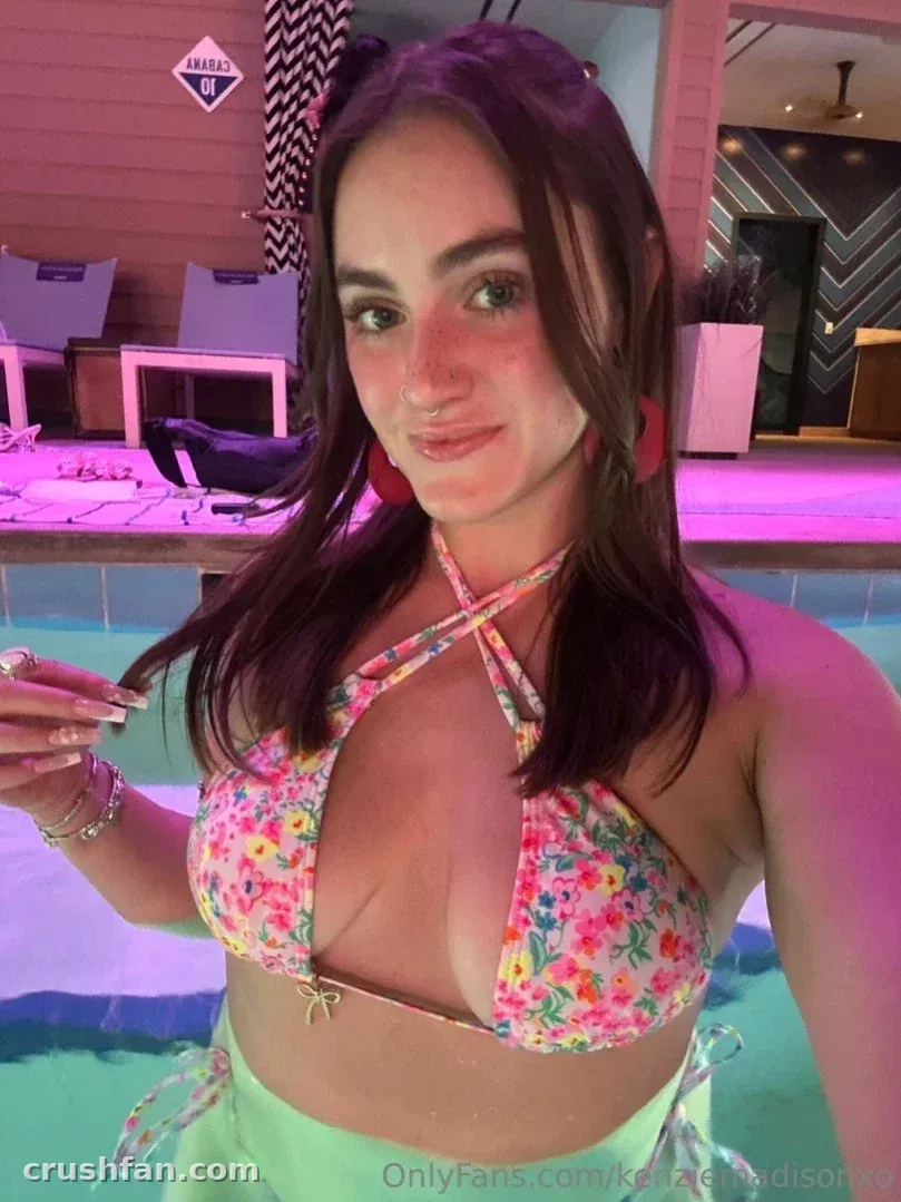 Kenzie Madison in a floral bikini top standing by an indoor pool with pink lighting