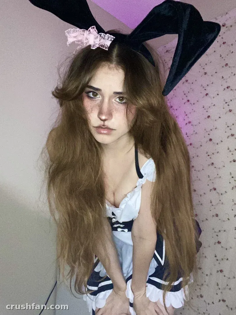 Creator wearing a black bunny ear headband and ruffled outfit indoors with soft pink lighting.