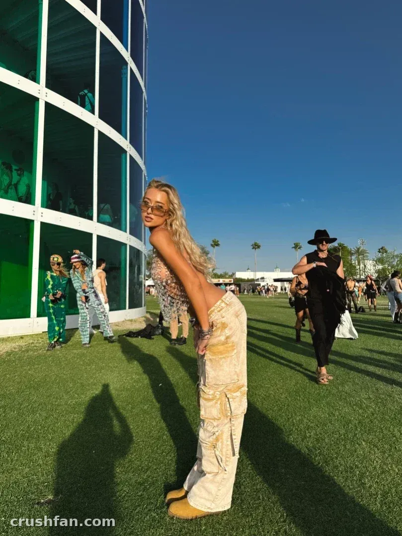 Madds con un top estampado y pantalones cargo claros inclinándose hacia delante sobre un césped soleado cerca de un edificio curvo de cristal
