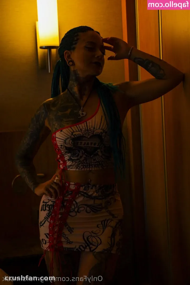 Mulher tatuada com um conjunto claro de estampa gráfica e cachecol azul-petróleo posando sob luz interna quente