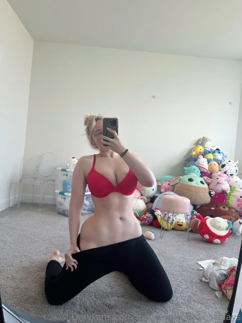 Linnea kniet auf einem Teppich in rotem BH und schwarzer Leggings und macht ein Spiegel-Selfie.