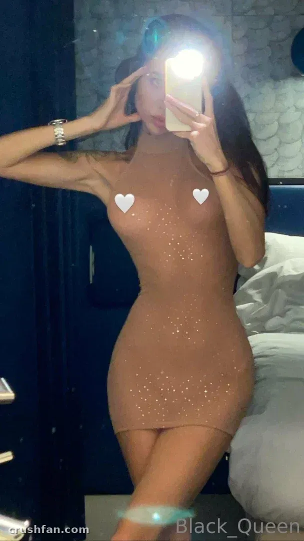 Darina con un vestido nude brillante tomándose una selfie en el espejo con un flash brillante en un dormitorio.