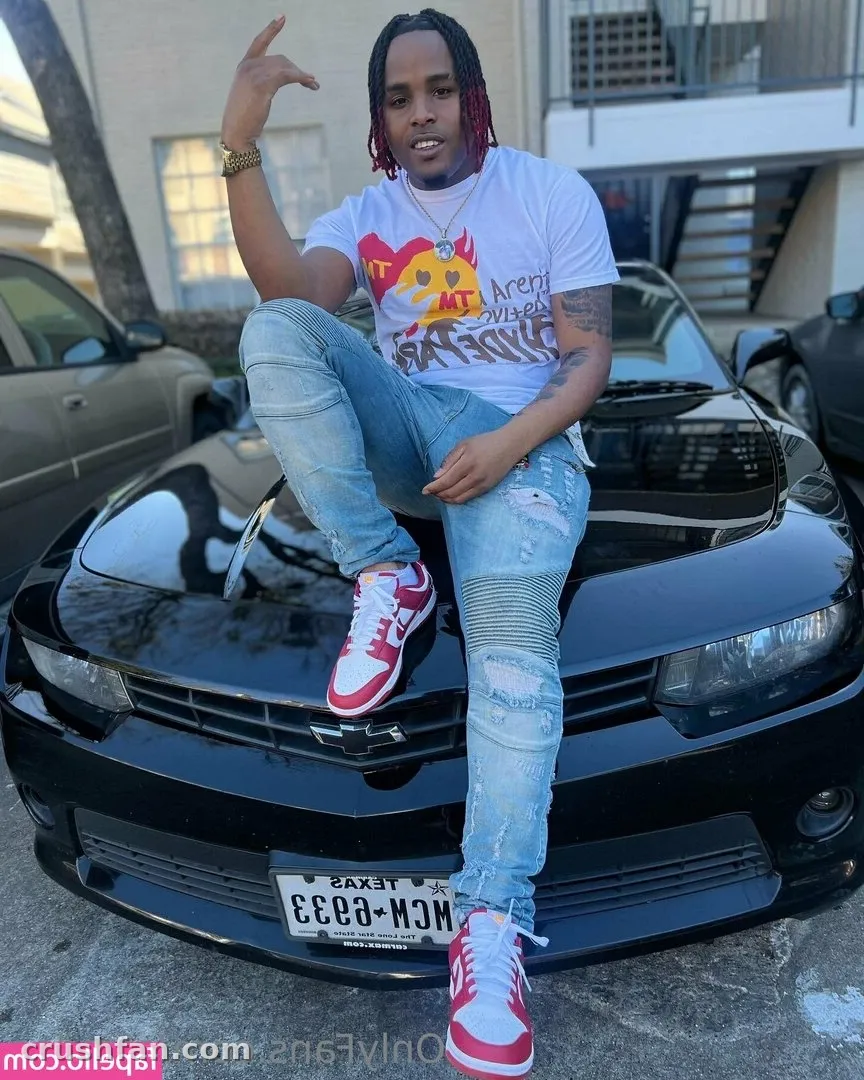 Dee sitting on a black car hood wearing a white graphic tee and light blue jeans.