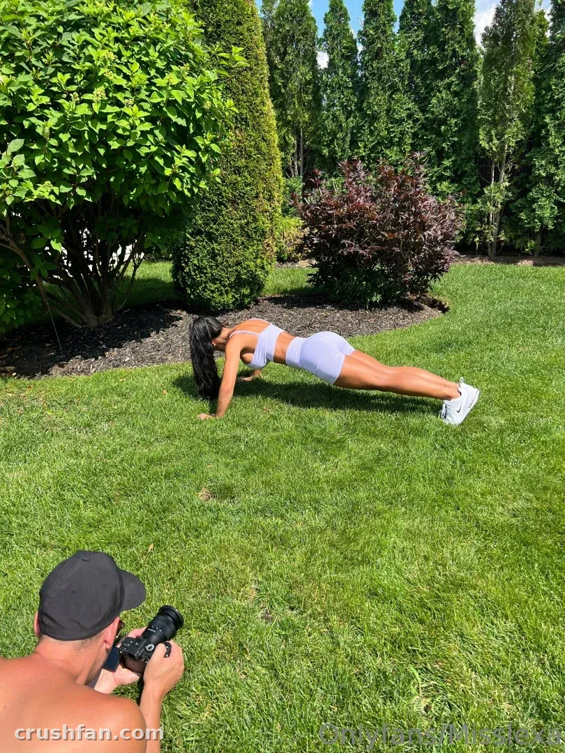 Miss Lexa holding a plank on a green lawn while a photographer films from the grass.
