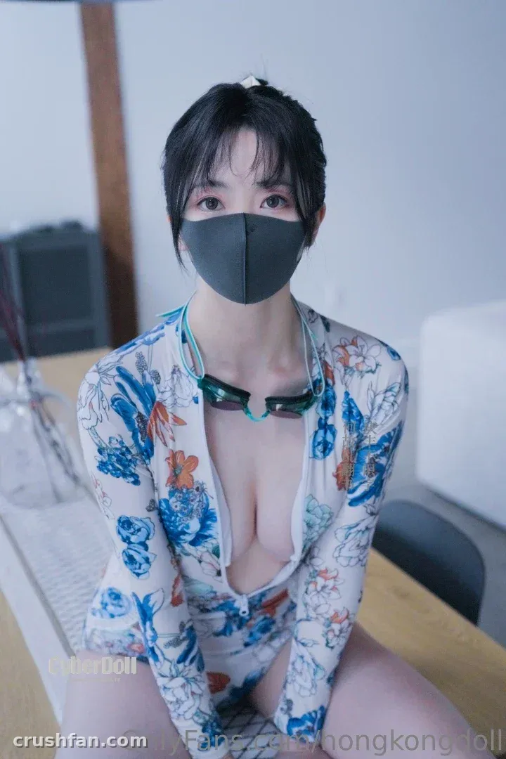 HongKongDoll in a floral bodysuit and black mask sitting at a desk in a bright room