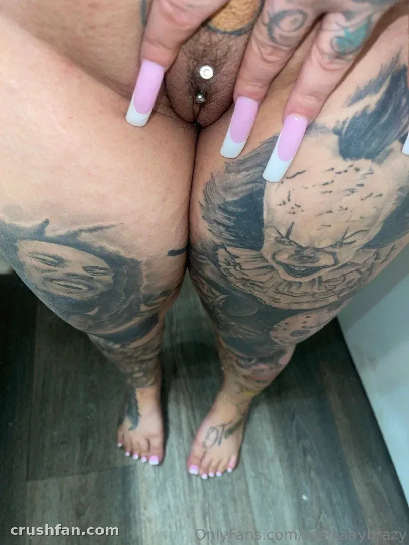 Vue plongeante des jambes de Kaay brazy montrant de grands tatouages et des ongles roses.