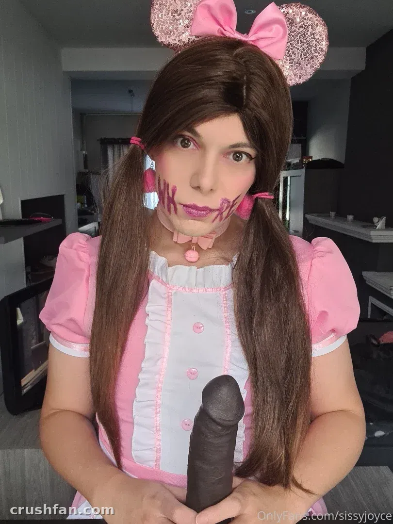 Sissy Joyce in a pink and white costume with pigtails and a large pink bow headband indoors.
