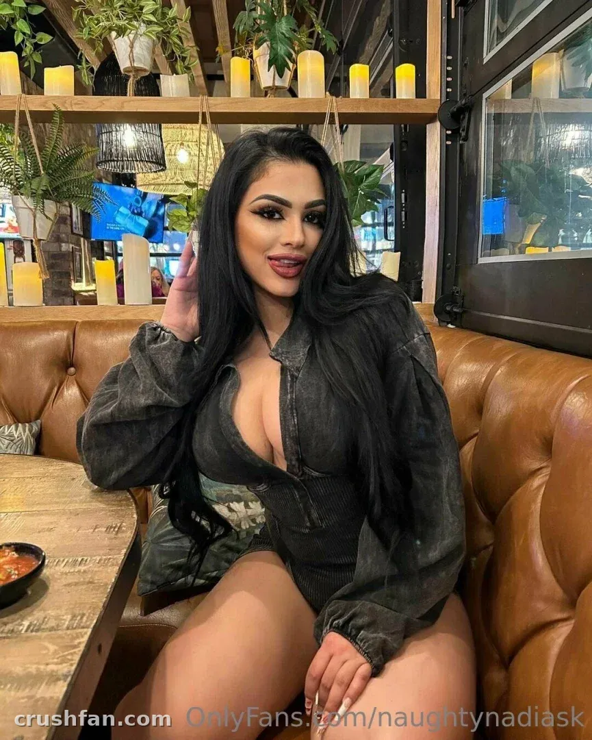 Nadia seated in a tan leather restaurant booth wearing a dark denim top, warm candlelight behind her