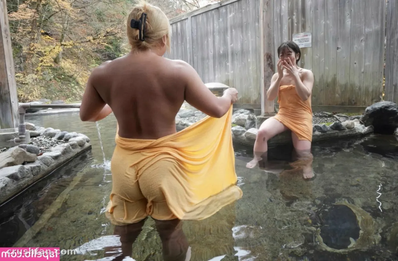Woman in a yellow towel standing in an outdoor hot spring with rocks and a wooden fence