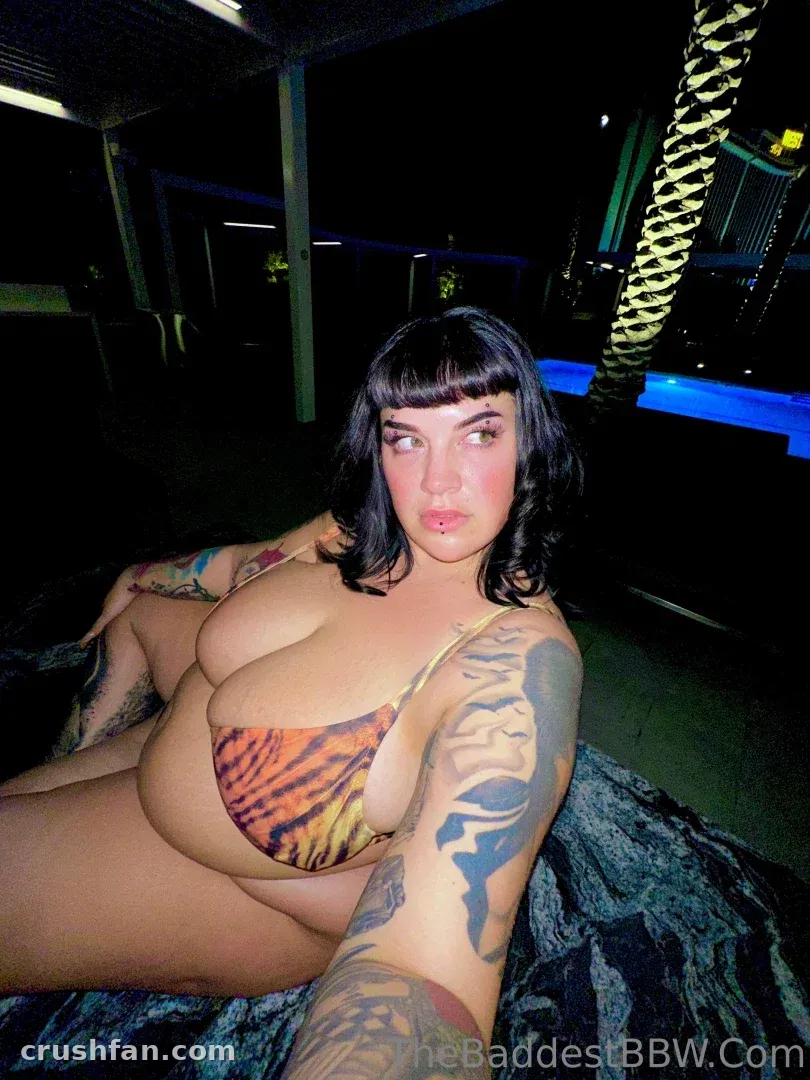 Marilyn Mayson con un bikini de estampado de tigre recostada en un entorno exterior con poca luz y luz azul.