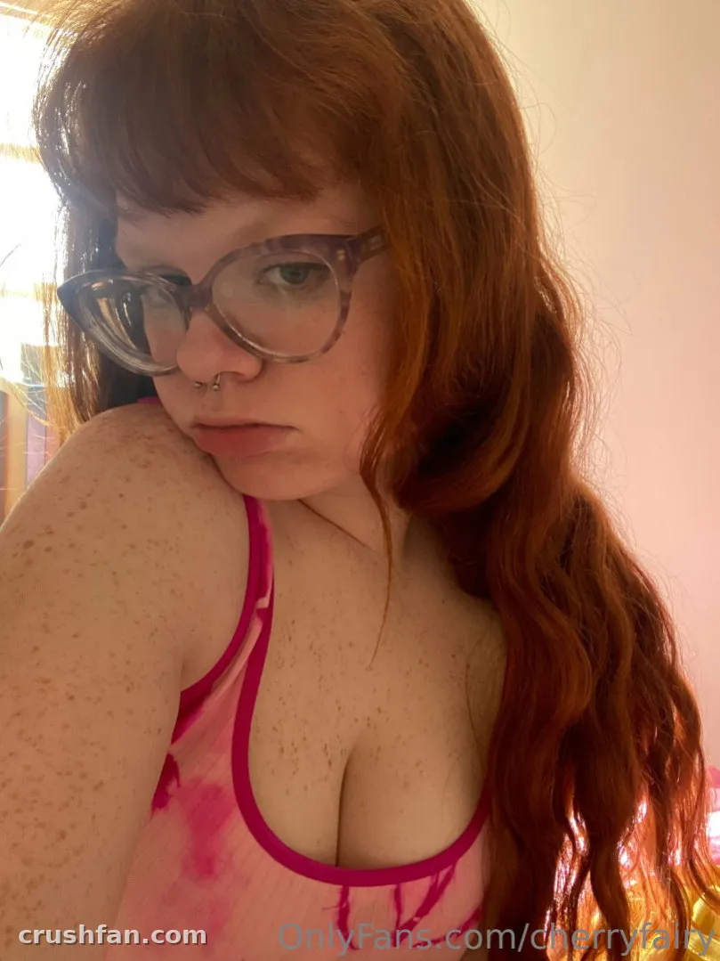 Creator Cherry in einem rosa Batik-Oberteil und gemusterter Brille, drinnen