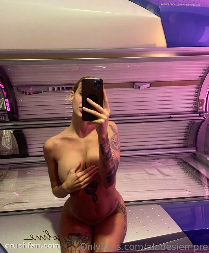 Anita tira uma selfie no espelho dentro de uma cama de bronzeamento iluminada em rosa