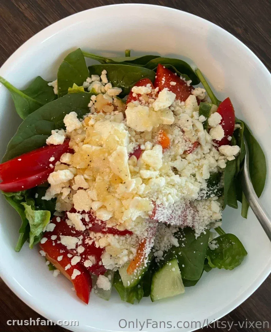 A white bowl filled with spinach salad topped with feta cheese and red peppers.
