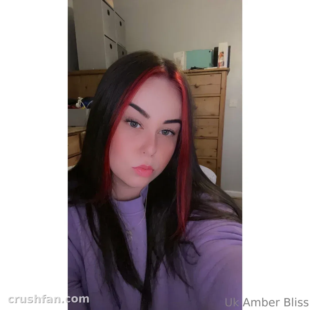Créatrice aux longs cheveux foncés et mèches rouges dans un haut lilas prenant un selfie en intérieur