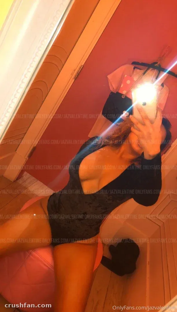 Latina Barbie en body sombre prenant un selfie miroir au flash dans une pièce aux tons chauds