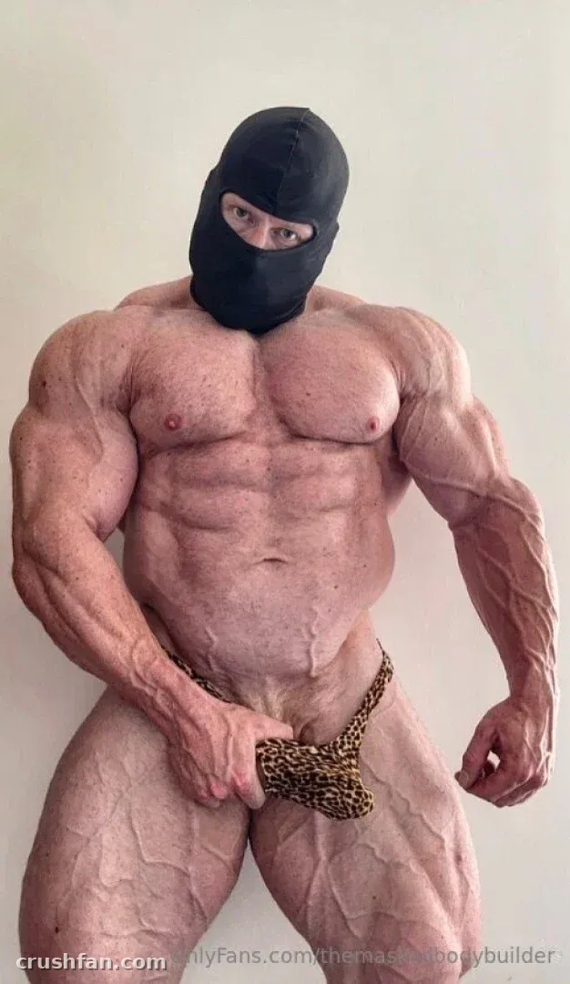 Muscular creator in a black balaclava and leopard-print pouch posing against a plain wall