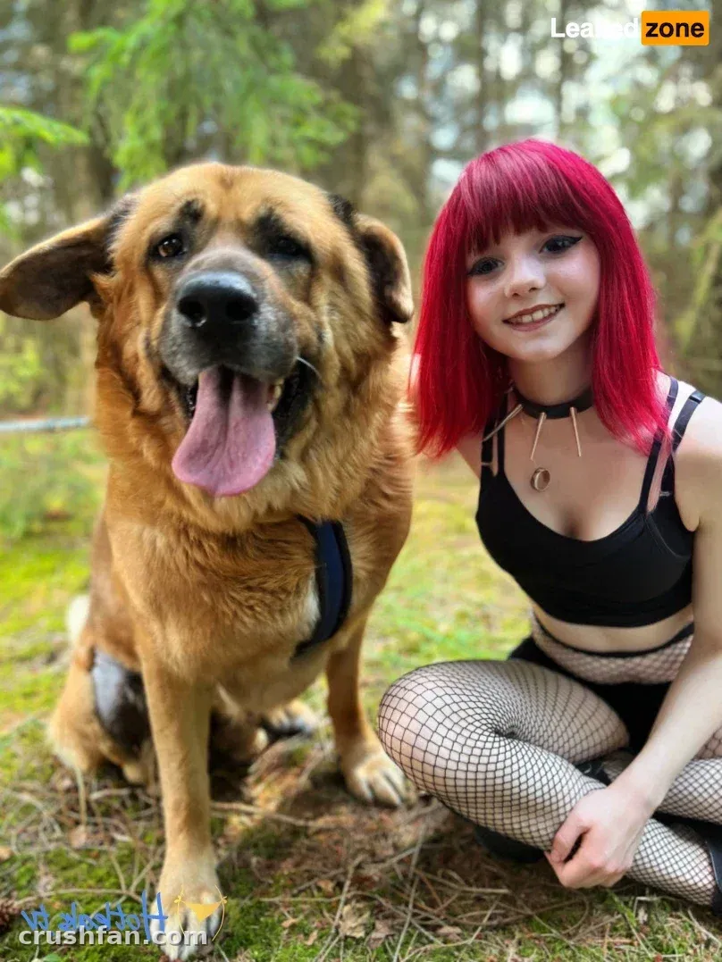 Creator with red bob hair kneeling beside a large tan dog in a green forest