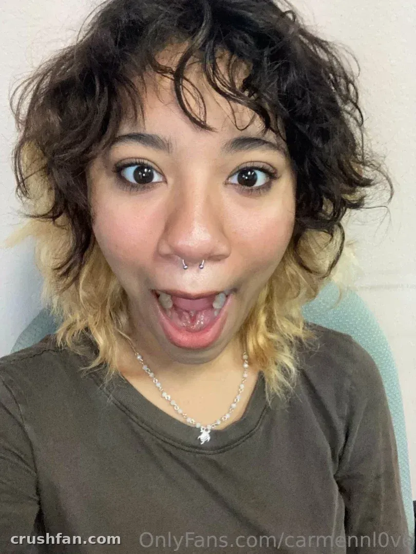 A oficial Carmen Love com uma blusa oliva e colar de prata, fazendo uma careta brincalhona em uma selfie em close-up em ambiente interno.