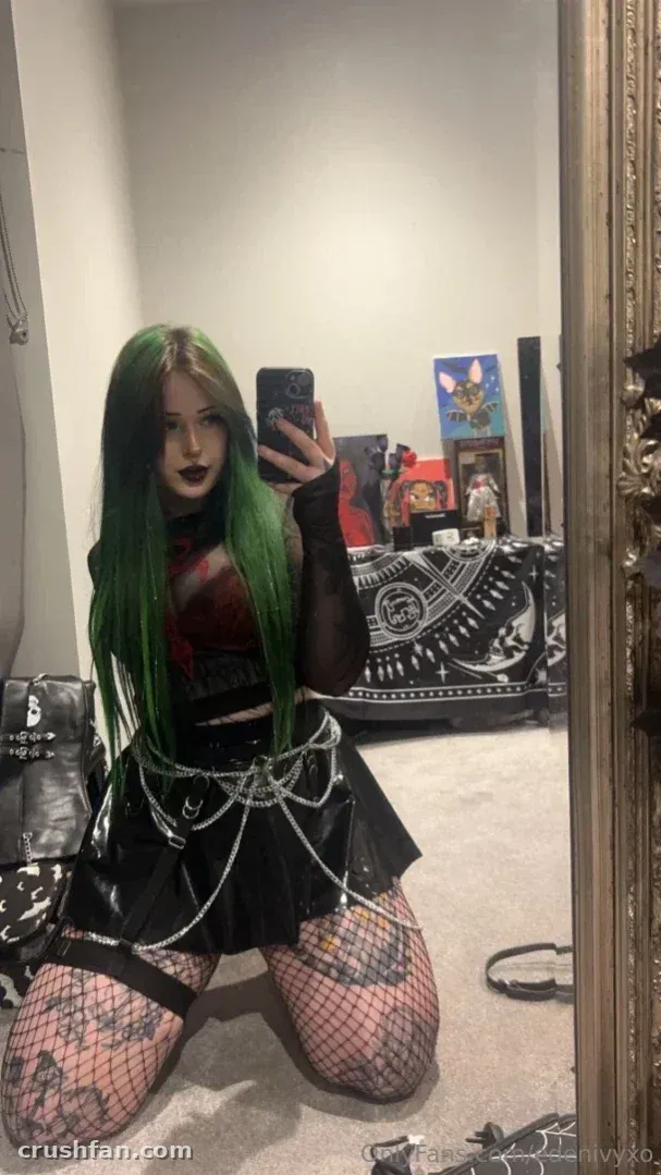 Eden takes a mirror selfie in a black outfit with silver chains and fishnet stockings.