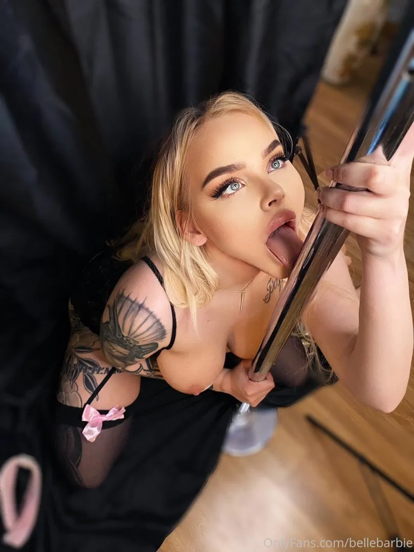 BELLEBARBIE holding a framed mirror while wearing a black outfit with a pink ribbon detail