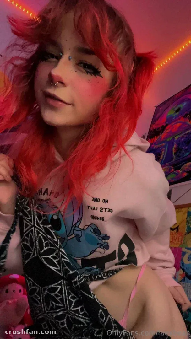 Fae de moletom rosa com cabelo ruivo, luzes neon rosa brilhando em um ambiente interno